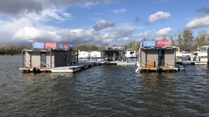 Una estructura flotante con varias cabañas, barcos amarrados y cielo despejado.