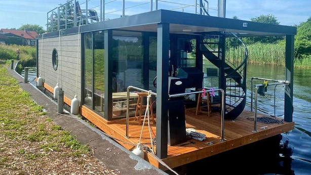 Ein modernes, schwimmendes Haus mit Glasfassade, einer Holzterrasse und einer Treppe zur oberen Terrasse.