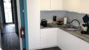 Una cocina compacta con armarios blancos, un hervidor negro y un lavamanos de acero inoxidable.