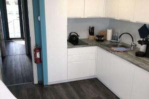 Una cocina compacta con armarios blancos, un hervidor negro y un lavamanos de acero inoxidable.