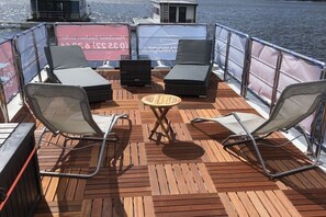 Eine Terrasse mit zwei Liegestühlen, einem kleinen runden Tisch und Blick auf das Wasser.