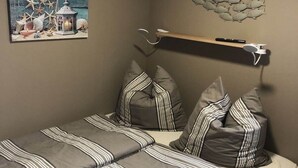Ein Schlafzimmer mit einem Bett, gestreiften Kissen, einem Wandregal mit einer Fernbedienung und einem Gemälde einer Küstenlandschaft.