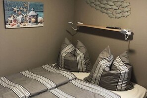 A bedroom with a bed, striped pillows, a wall-mounted shelf with a remote control, and a painting of a coastal scene. - myHolidayBoat Krimnicksee (Königs Wusterhausen)