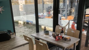 Ein Tisch mit Stühlen, eine Flasche und eine Tüte Snacks in einem Raum mit großen Fenstern mit Blick auf einen Steg.