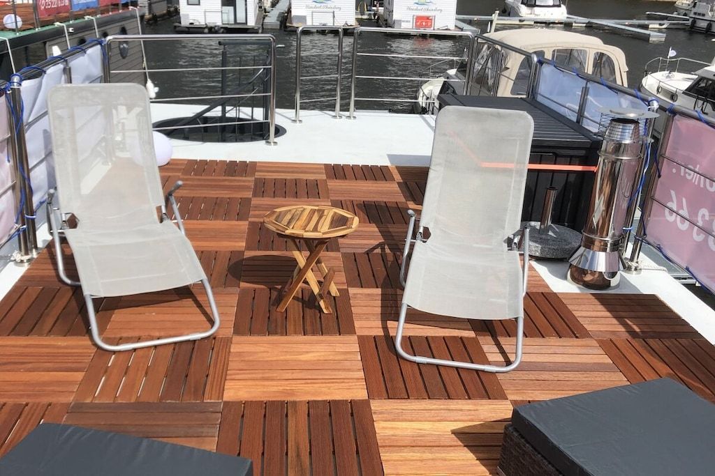 Ein Bootsdeck mit zwei Liegestühlen, einem kleinen Holztisch und einem Metallgrill.