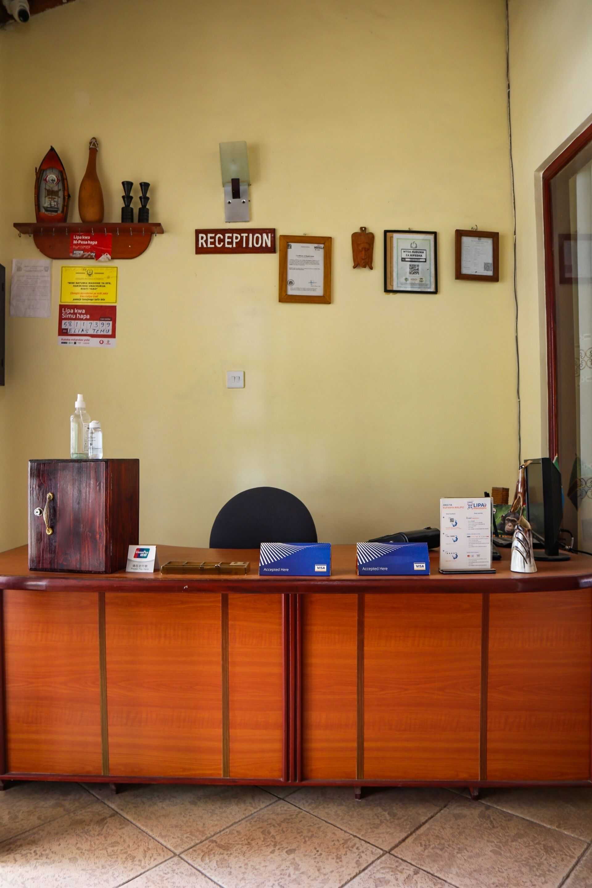 Mostrador de recepción con detalles de madera, una silla, un monitor de computadora y varios carteles y certificados en la pared.