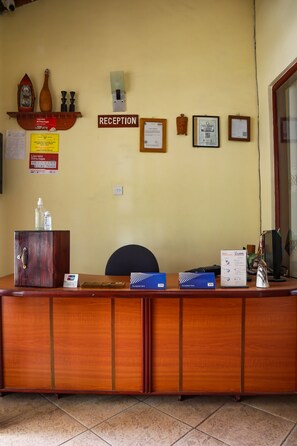 Mostrador de recepción con detalles de madera, una silla, un monitor de computadora y varios carteles y certificados en la pared.