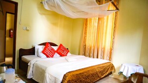 A hotel room with a bed, a bedside table, a chair, a small table, and a decorative canopy. - Rainbow Executive Lodge (Boma Ng'ombe)