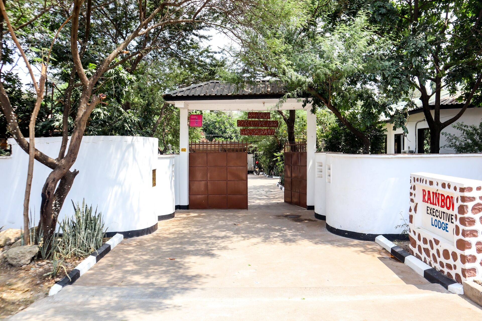 Een hek afsluit de toegang tot een pand met een bord waarop 'Rainbow Executive Lodge Restaurant' staat.