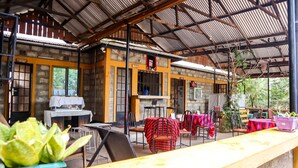 An outdoor cafe with tables and chairs, a coffee station, and a stone wall. - Rainbow Executive Lodge (Boma Ng'ombe)