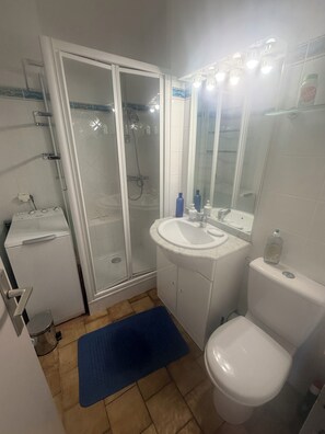 Ett badrum med en dusch som är avskärmad med glasväggar, ett vitt handfat, en toalett och en blå badrumsmatta.