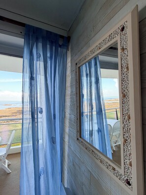 Une pièce dotée d’une grande fenêtre, d’un miroir avec un cadre décoratif et d’un rideau léger orné de motifs de papillons.