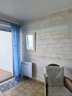 Ein Zimmer mit einem Korbstuhl, einem Heizkörper, einem Fenster mit Blick und einer gemusterten Matte auf dem Boden.