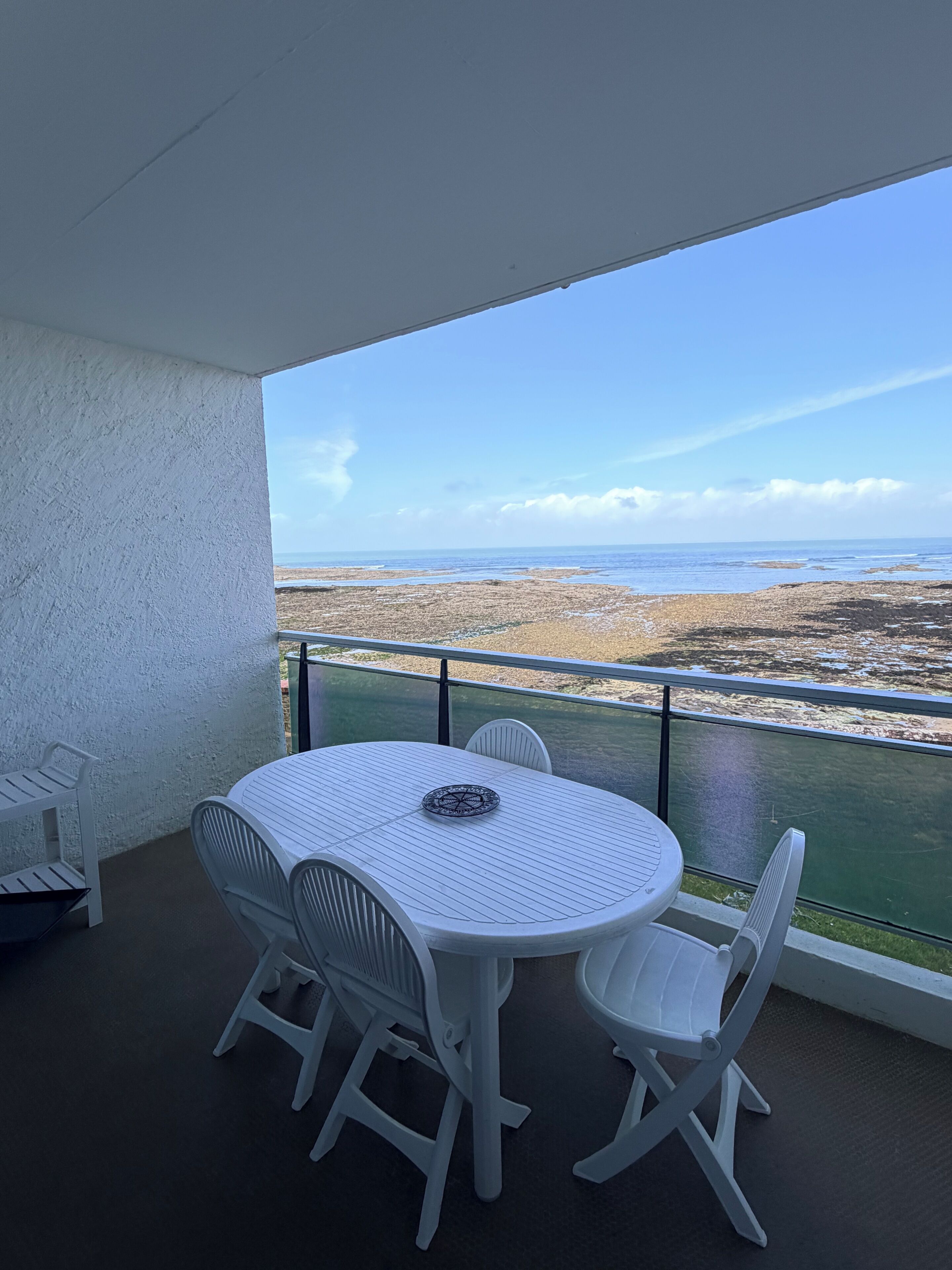 Ein Balkon mit weißem Tisch und Stühlen, der auf eine Küstenlandschaft blickt.