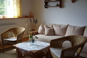 A cozy living room with a sofa, two wicker chairs, a table with a vase, and a window with curtains. - under the old apple tree (Unterspreewald OT Leibsch)