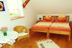 A bedroom with two beds, a wicker chair, a small table with a vase, and a window. - under the old apple tree (Unterspreewald OT Leibsch)