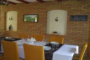 A dining area with a brick wall, two wall-mounted sconces, a framed landscape painting, and a table set for four with chairs. - under the old apple tree (Unterspreewald OT Leibsch)