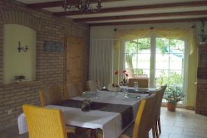 A dining area with a brick wall, a wooden door, a table set for four, and a potted plant. - under the old apple tree (Unterspreewald OT Leibsch)
