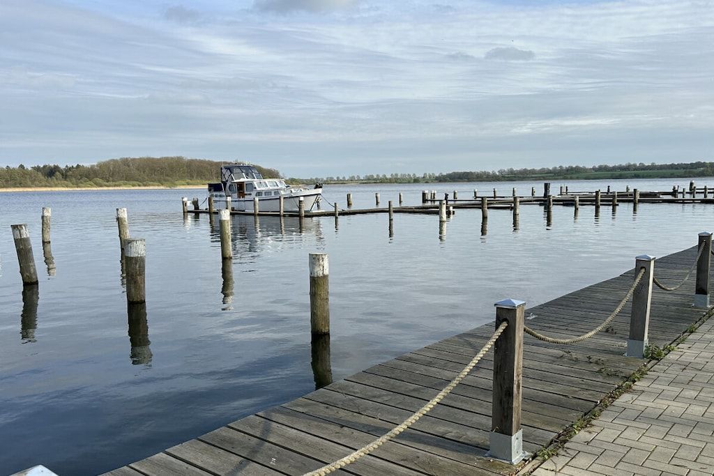A calm lake with a dock extending into the water, wooden posts, and a boat moored at the dock.
