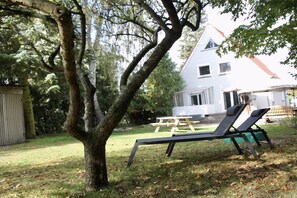 Un pati envoltat d'arbres amb gespa, una taula de picnic de fusta i dues cadires relaxants negres.