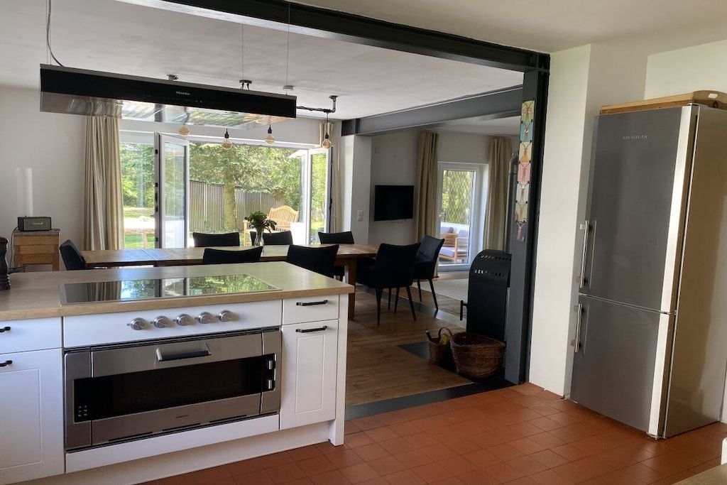 Une cuisine moderne équipée d’un four encastré, d’un réfrigérateur et d’un coin repas avec une table et des chaises.