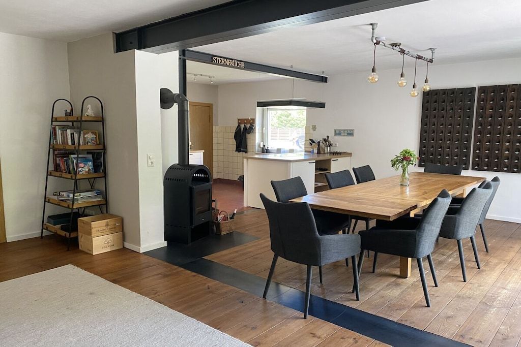 A modern kitchen with a central island, a dining area with a wooden table and chairs, and a bookshelf.