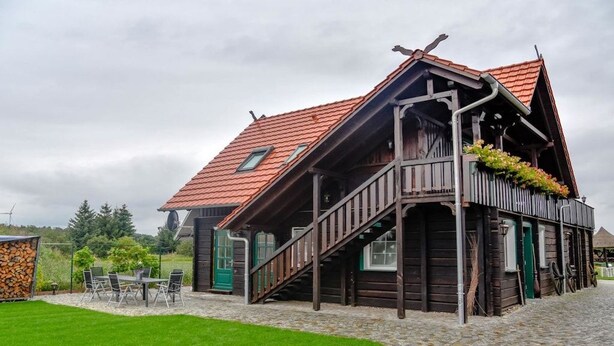 Een traditioneel houten huis met een schuin dak, een trap die naar een veranda leidt, en een patio met stenen bestrating.