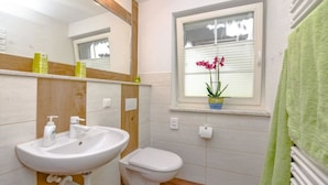 Een badkamer met een wit wastafelmeubel, toilet, spiegel en een raam met zonwering.