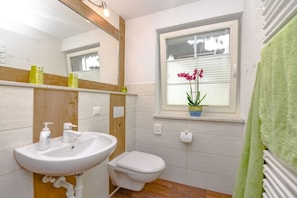 Un bagno con un lavandino bianco, un water, uno specchio e una finestra con persiane.