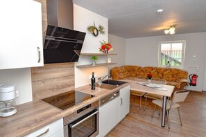 A compact kitchen with a built-in oven, a coffee maker, and a dining area with a table and chairs. - Holiday apartment with 2 bedrooms (Märkische Heide OT Biebersdorf)