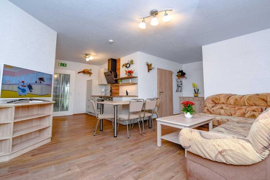 Ein modernes Wohnzimmer mit einer Couch, einem Couchtisch und einem Fernseher auf einem Schrank. Es gibt einen Essbereich mit Tisch und Stühlen.