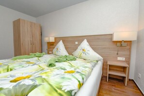 A bedroom with a bed, a wooden wardrobe, a nightstand with a lamp, and a wall-mounted light. - Holiday apartment with 2 bedrooms (Märkische Heide OT Biebersdorf)