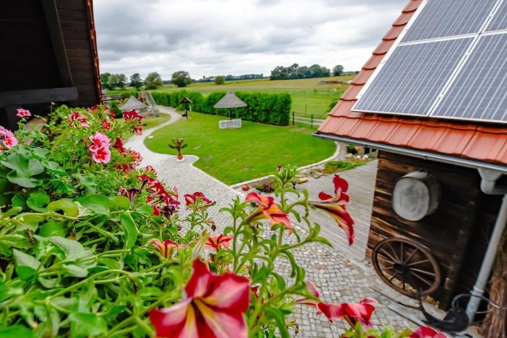 A garden pathway leading to a green lawn with a gazebo, surrounded by flowering plants and a solar panel on the roof.