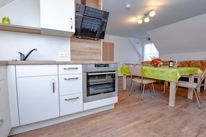 A modern kitchen with white cabinetry, a built-in oven, and a dining area with a table set for four. - Holiday apartment with 2 bedrooms (Märkische Heide OT Biebersdorf)