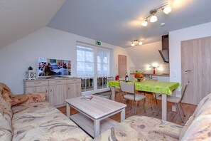 A cozy living area with a sofa, a coffee table, and a dining table with chairs. There is a television on a cabinet, and a kitchen area is visible in the background. - Holiday apartment with 2 bedrooms (Märkische Heide OT Biebersdorf)