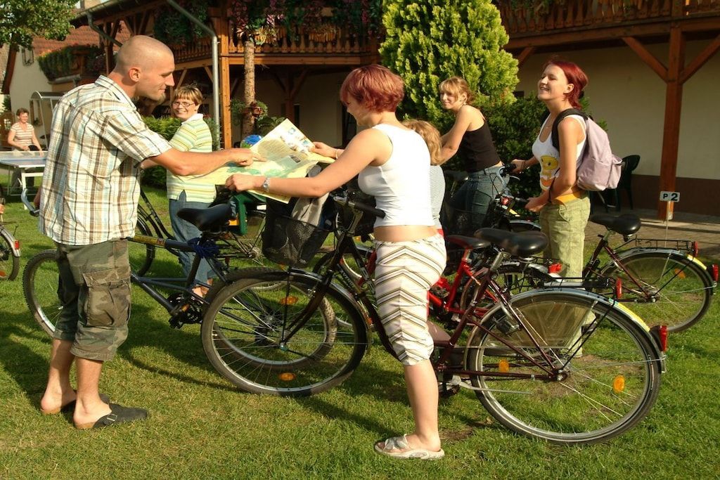 Um grupo de pessoas ao ar livre com bicicletas, uma estrutura de madeira ao fundo e uma placa indicando vaga de estacionamento P2.