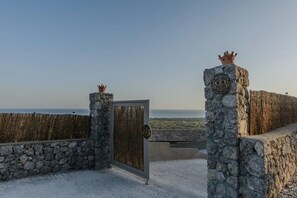 Een stenen poort met een kroonembleem, die uitkomt op een uitzicht over de zee.
