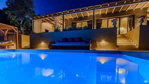 A swimming pool with a patio area, a staircase, and a seating area with cushions.