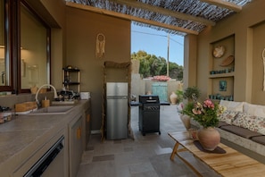 A compact kitchen with a built-in refrigerator, a gas stove, and a sink. There is a dining area with a wooden table and a sofa. - AETHER - Romantic Private Pool Villa with Spectacular Ocean Views (Corfu)
