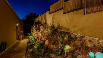Un área de jardín ajardinada con un muro de piedra, plantas en macetas y un sendero que conduce a la entrada de un edificio.