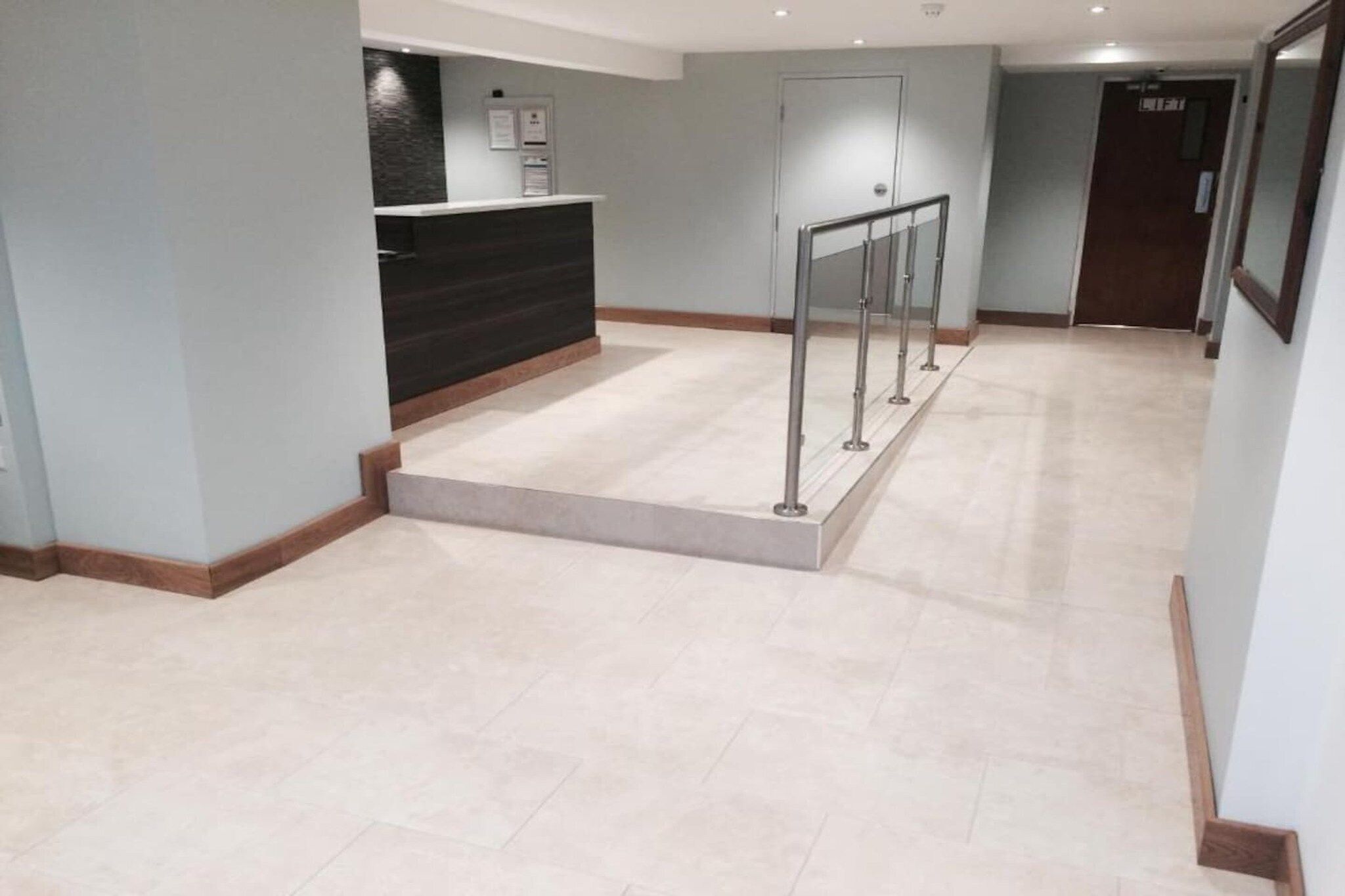 A hotel reception area with a reception desk, a staircase, and a door in the background.