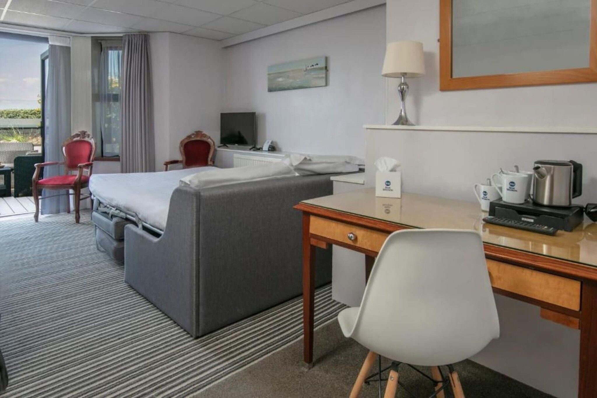 Ein Hotelzimmer mit einem Bett, einem Schreibtisch, einem Sessel, einem Fernseher und einem Fenster mit Vorhängen.