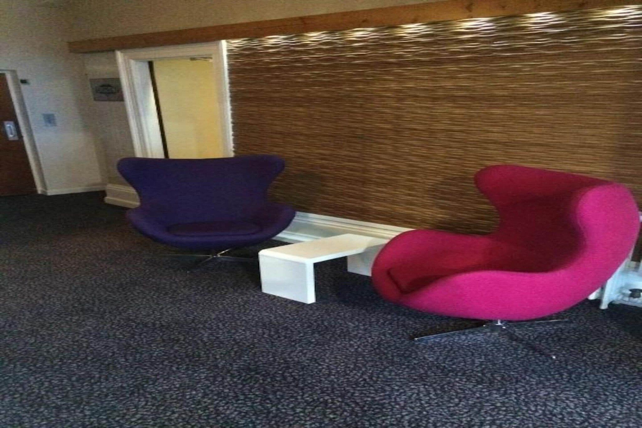 A room with two chairs, one purple and one red, and a small white table between them.