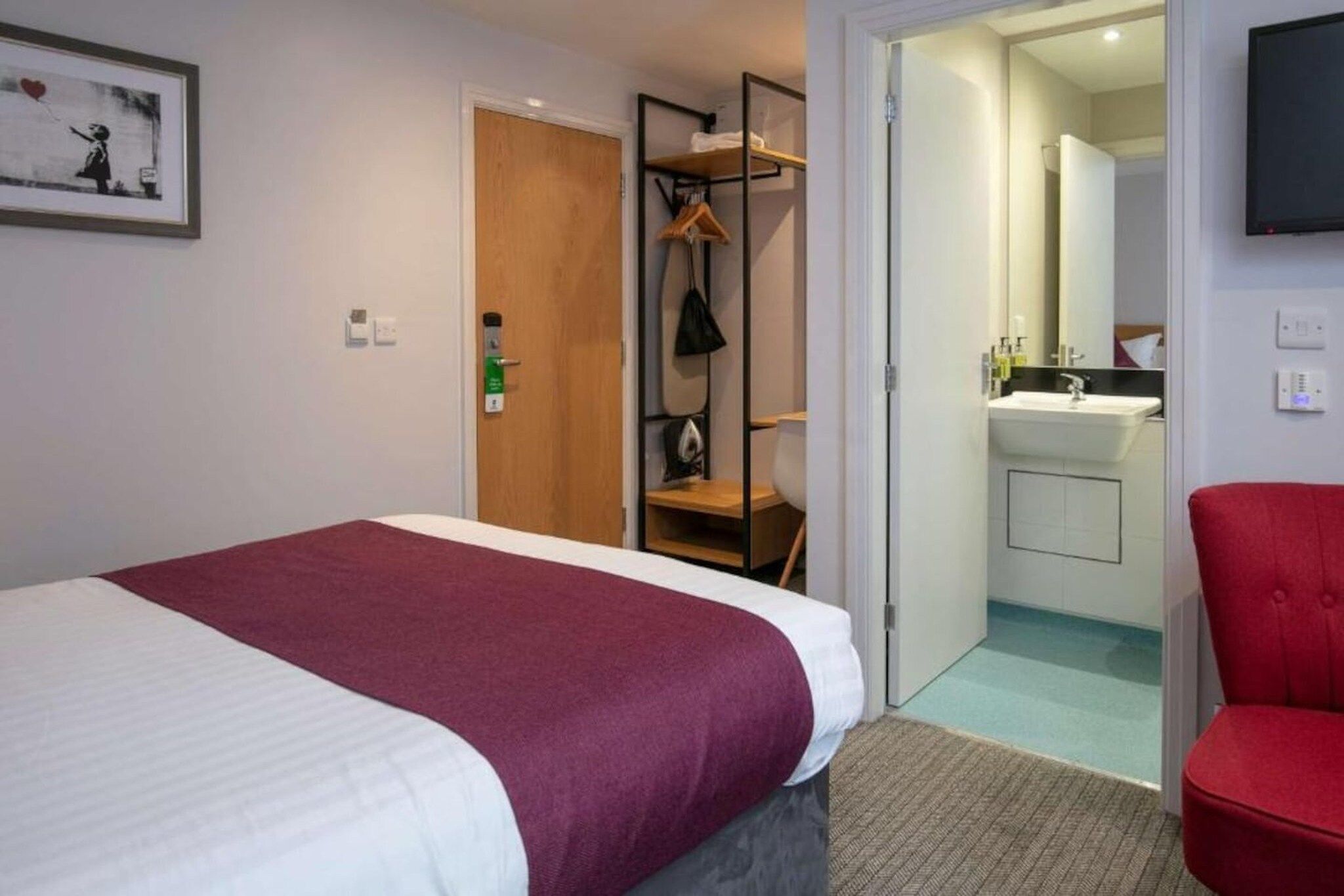 A hotel room with a bed, a red chair, a bathroom with a sink, and a shower.