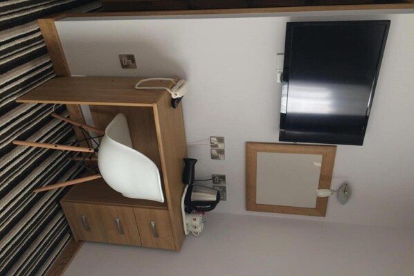 Una habitación con un armario de madera, una silla blanca, un televisor de pantalla plana montado en la pared y un espejo pequeño.