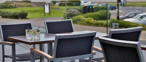 Espace extérieur aménagé avec des tables et des chaises, vue sur la route et présence de verdure.