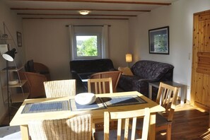 A room with a dining table, chairs, a sofa, a lamp, and a window with curtains. - Holiday apartment with 2 bedrooms (Zislow)