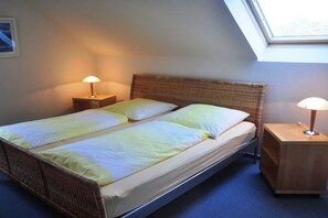 Una cama doble con cabecera, dos mesitas de noche con lámparas y un tragaluz arriba.