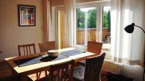 Ruokailutila, jossa on puinen pöytä, tuolit ja suuret ikkunat, joista on näkymä ulos.