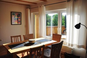 Un comedor con mesa de madera, sillas y vistas al exterior a través de amplios ventanales.
